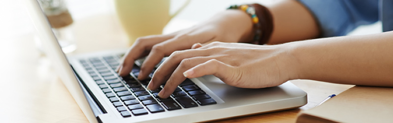 Show hands typing on a laptop computer on a desk